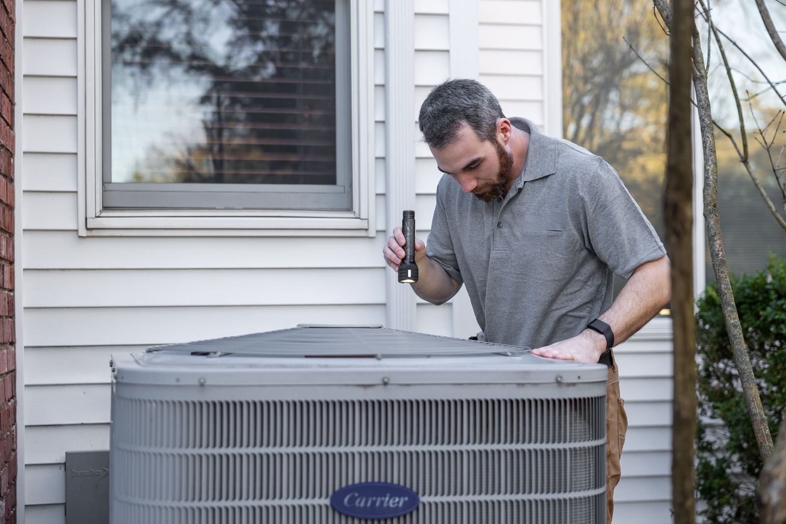 HVAC installer looking over an outdoor air conditioning condenser beside a house