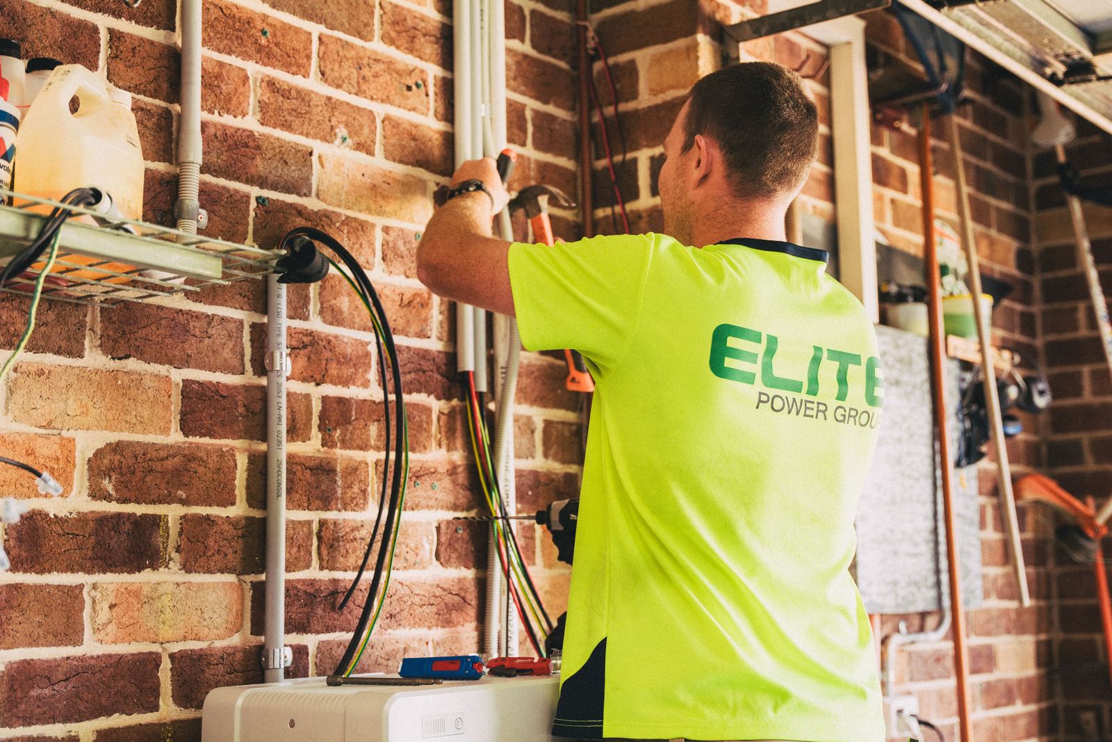 Installer routing electrical wires through grey conduit on a brick wall for new HVAC equipment