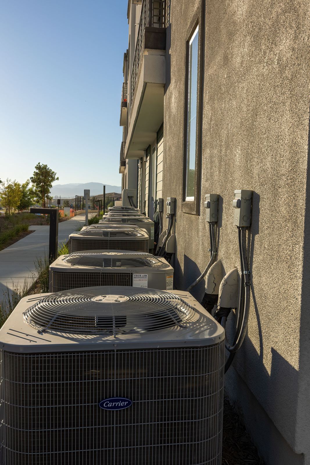 Row of outdoor condensing units with individual electrical disconnects along a multi-unit building
