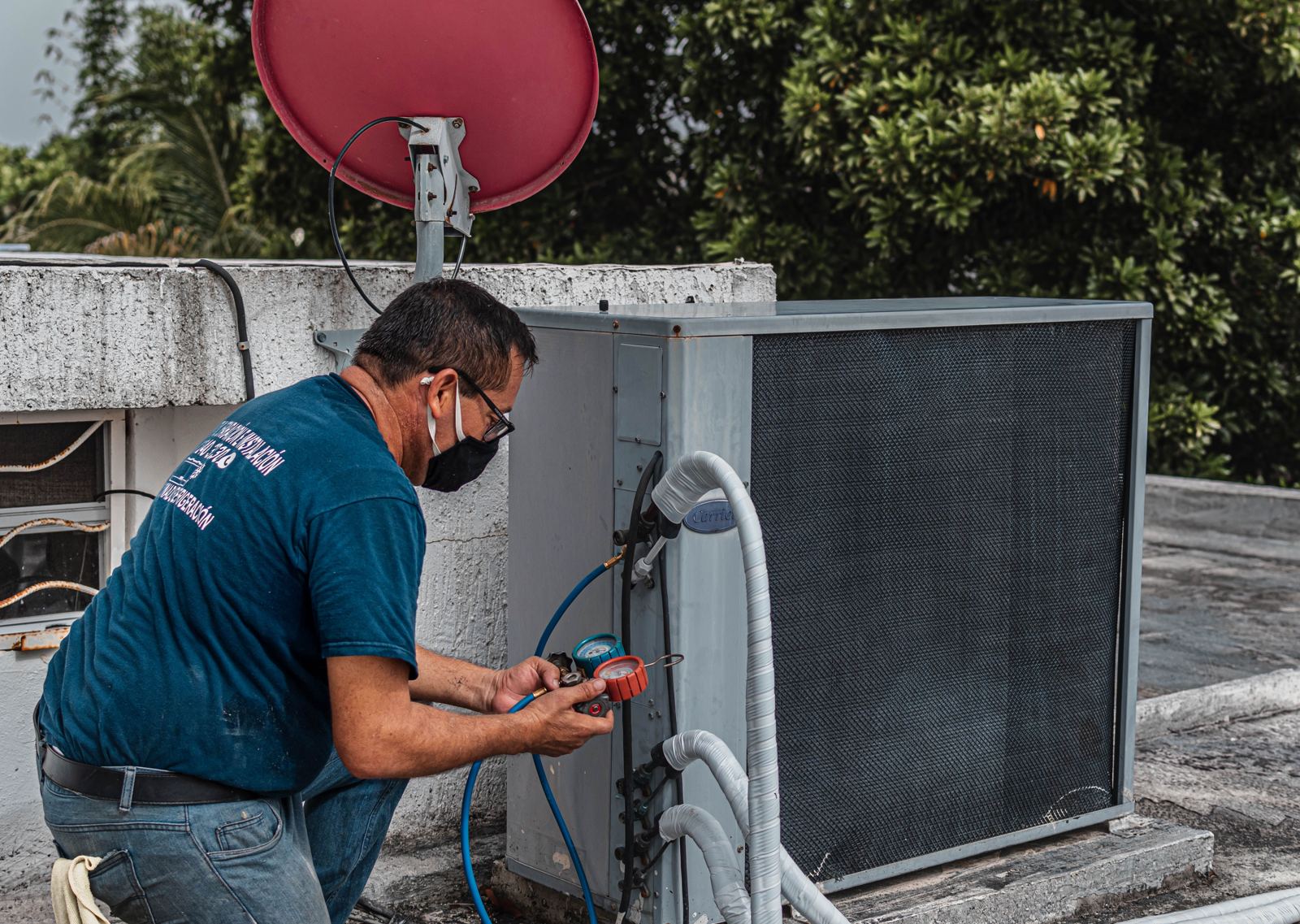 Technician checking a rooftop cooling unit with manifold gauges