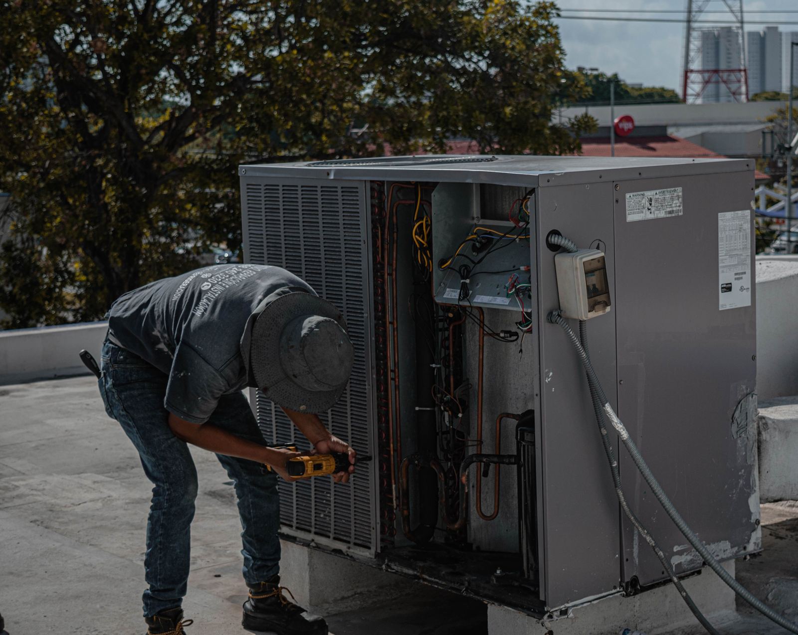 Technician using a drill on a rooftop packaged HVAC unit with the side panel removed